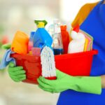 woman-rubber-gloves-holding-basin-with-detergents-blurred-background-min